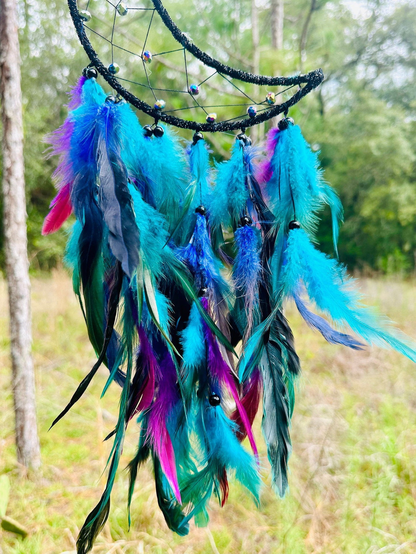 Crescent moon dream catcher featuring layered blue and purple feathers on black ring