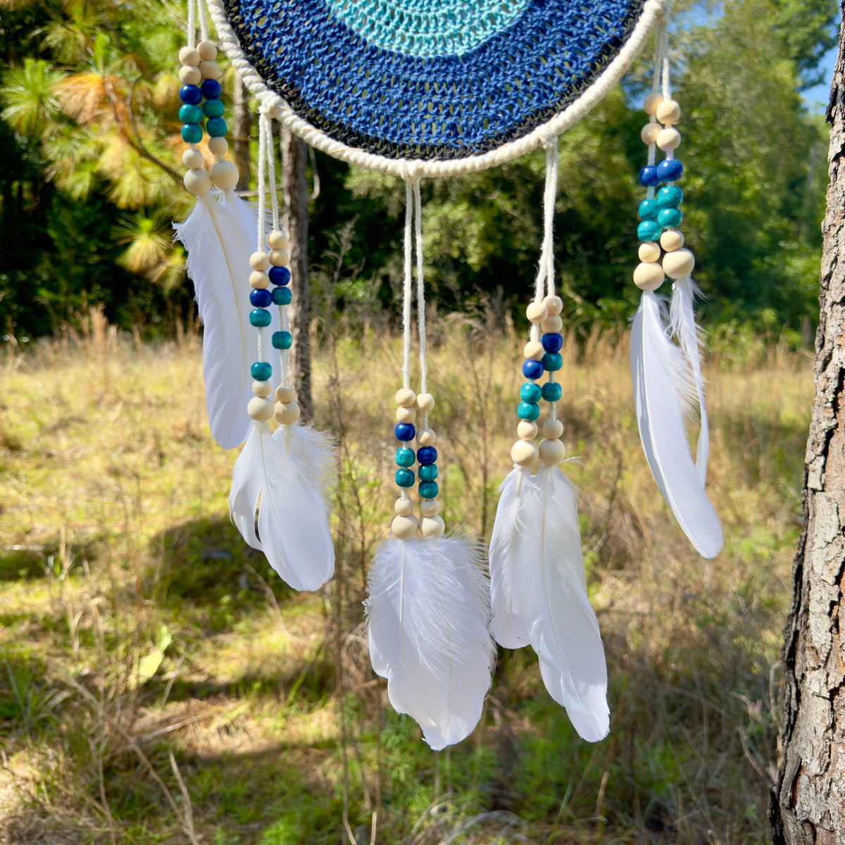 Beaded evil-eye wall hanging detail: blue beads and white feathers on dangling cords