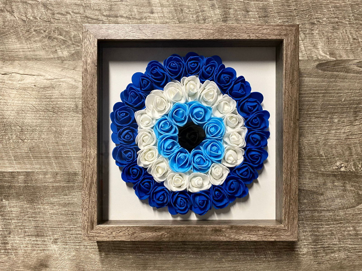Brown wood-framed shadowbox with blue and white rosette evil eye flower wreath
