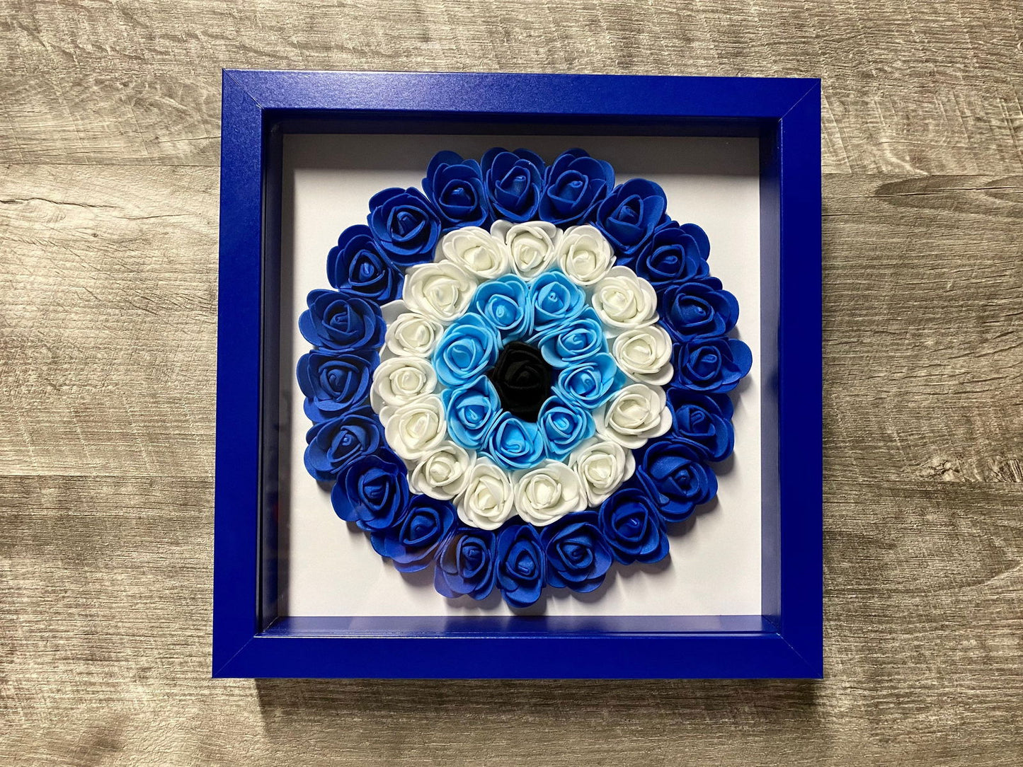 Blue-framed shadowbox with blue and white rosette evil eye flower wreath
