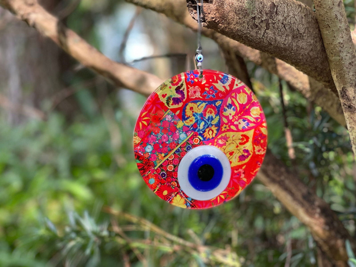 Evil eye wall hanging with red and blue mosaic pattern, hanging on a branch.