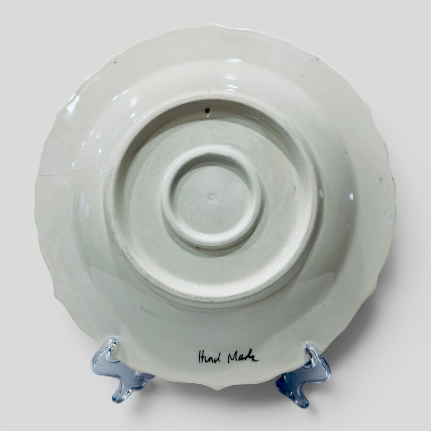 Ceramic plate back with round center well and handwritten base mark, mounted on blue feet