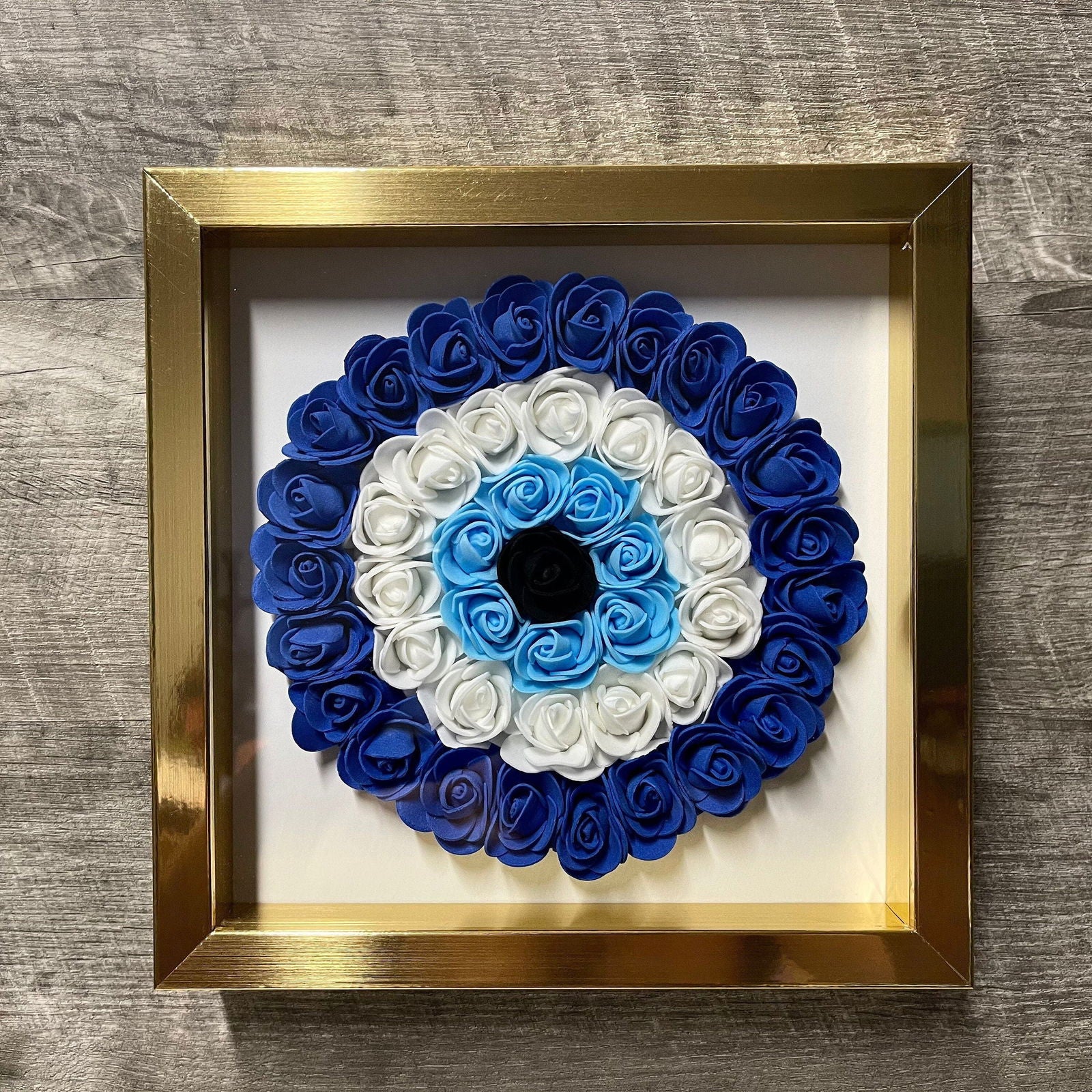 Gold-framed shadowbox with blue and white rose evil eye floral centerpiece