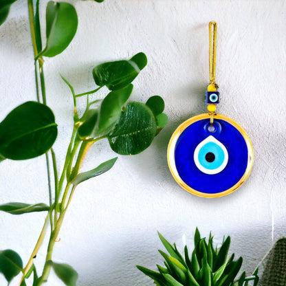 Blue evil eye charm with gold rim and hanging cord on wall