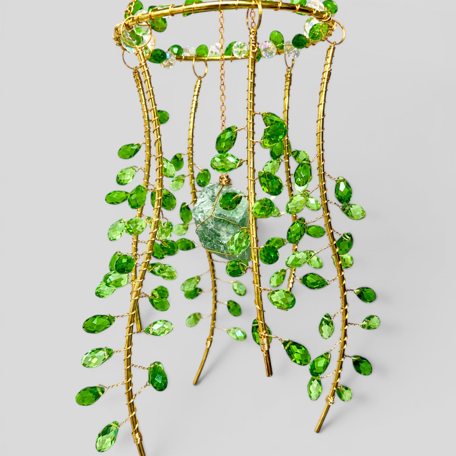 Hanging gold metal suncatcher with green beads and a clear faceted stone center