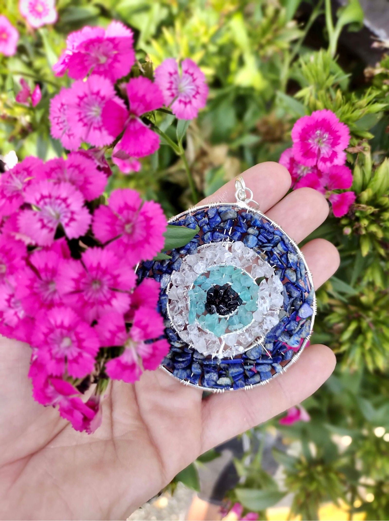 Round evil eye pendant in hand, blue beaded border and aqua eye with silver loop