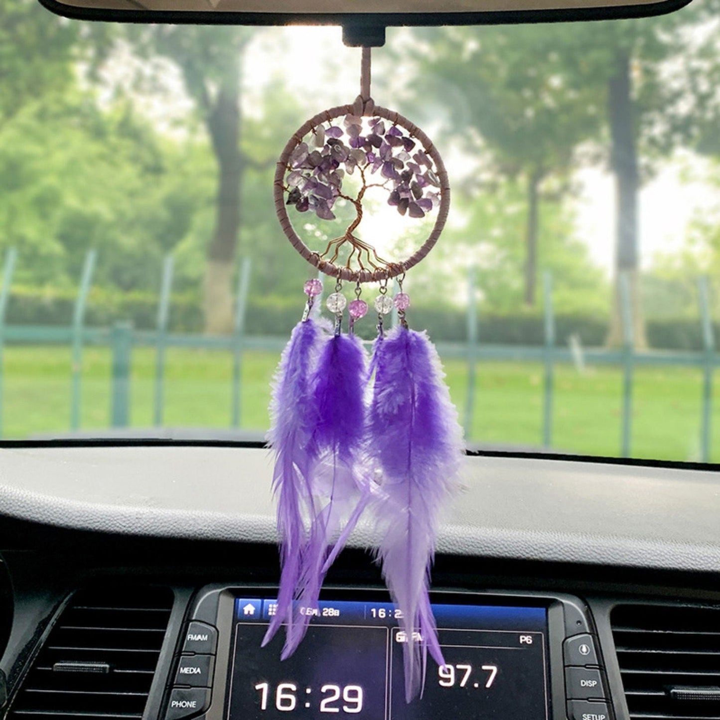 Purple dreamcatcher hanging from a car rearview mirror, round amethyst tree design with feathers