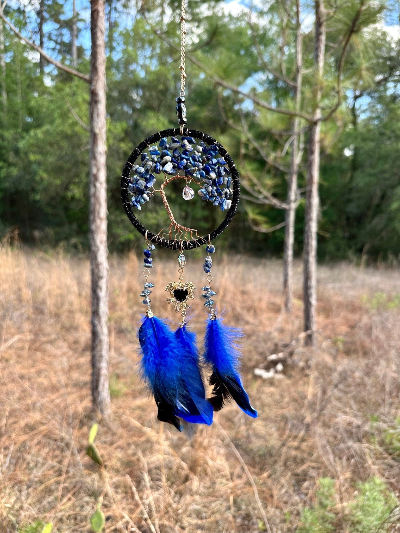 Blue beaded dreamcatcher with gold chain, blue feathers, and black center accent