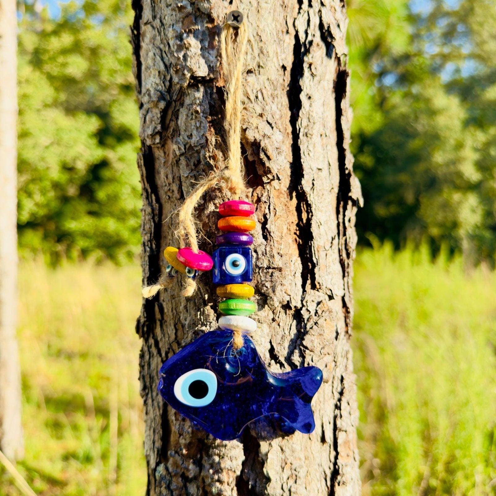 Blue fish evil eye wall hanging with colorful wood beads and rope tassel on bark