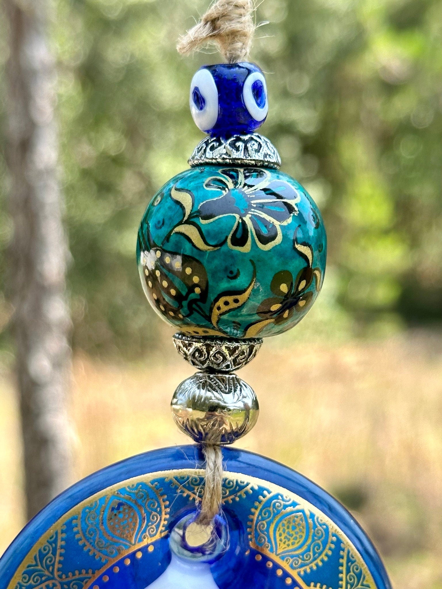 Close-up of ceramic evil eye wall hanging with teal patterned bead and blue painted disk