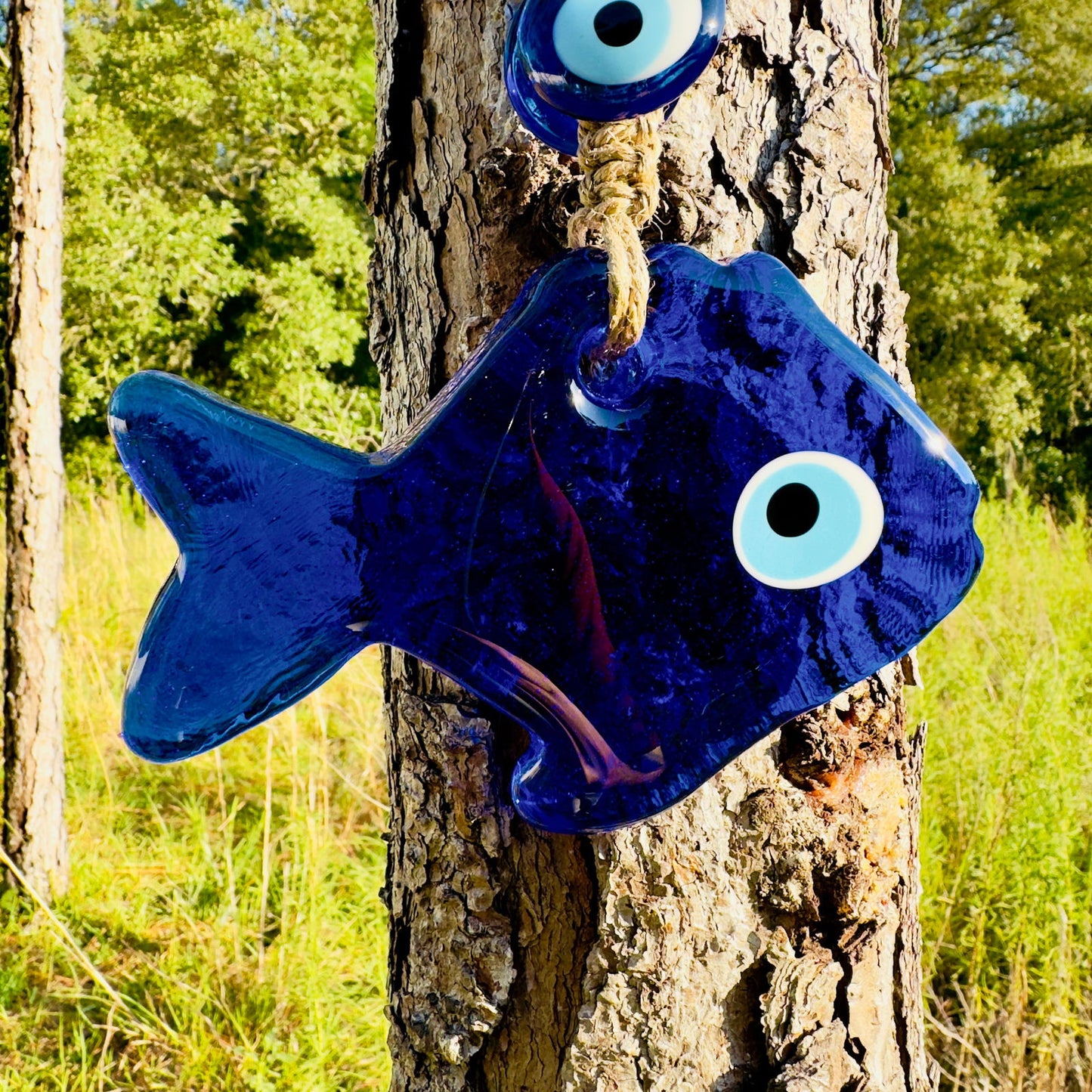 Blue fish wall charm with large evil eye bead, macrame ties hanging on bark
