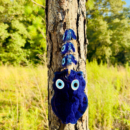 Blue evil-eye owl wall hanging macrame, hanging from rope on tree trunk