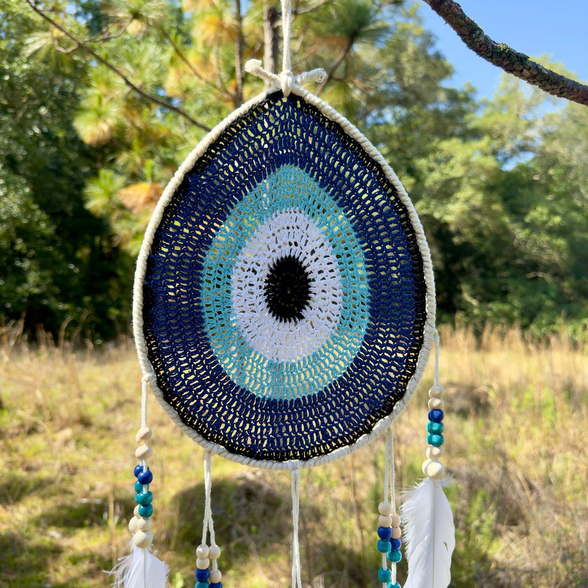 Teardrop evil-eye crochet wall hanging with blue and aqua concentric pattern, white feathers