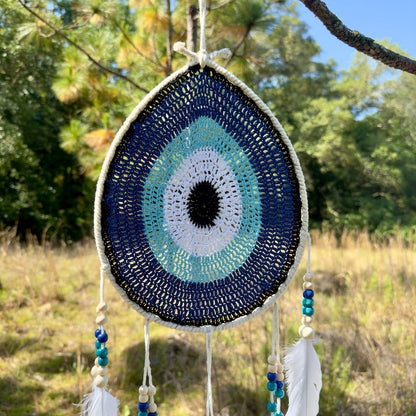 Teardrop evil-eye crochet wall hanging with blue and aqua concentric pattern, white feathers
