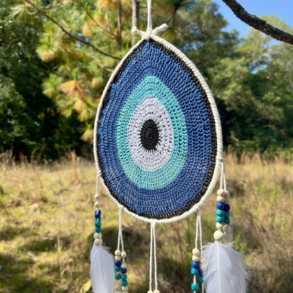 Teardrop evil-eye wall hanging with blue/aqua concentric beaded crochet and hanging feathers